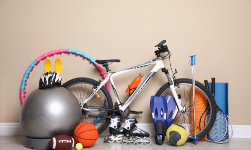 Bicycle and different modern sport equipment near beige wall